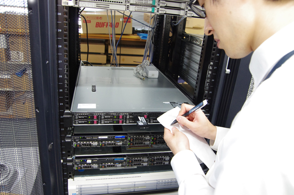 フロントエンド‗サーバー前でメモをとる若手社員